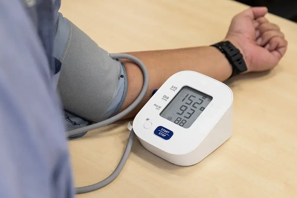 Digital blood pressure monitor wrapped on a patient’s arm, displaying 152/93 and pulse on the screen.